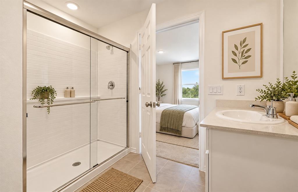 Bathroom featuring a walk-in shower with a glass enclosure, white tile surround, vanity with stone-style countertop, and drop-in sink