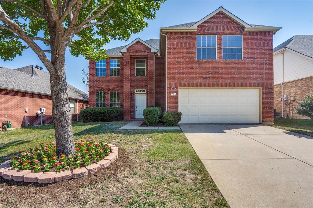 Two-story brick exterior featuring a multi-gabled roofline, concrete driveway, and a custom circular flower bed with stone edging