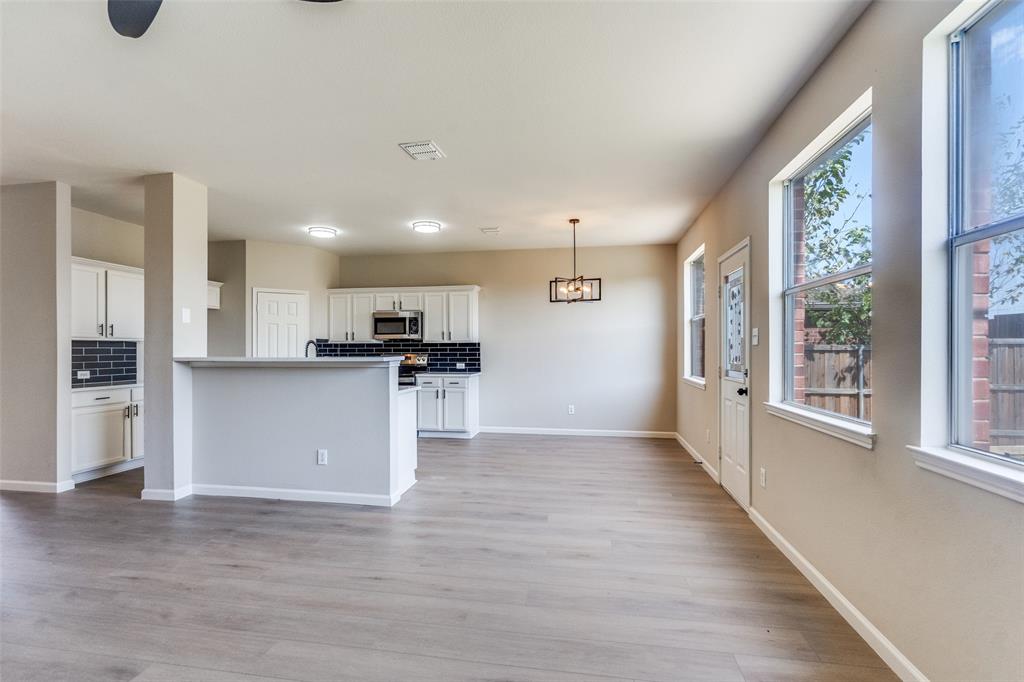 Kitchen featuring white cabinetry, dark tile backsplash, stainless steel microwave, wood-finish flooring, and a pendant light fixture
