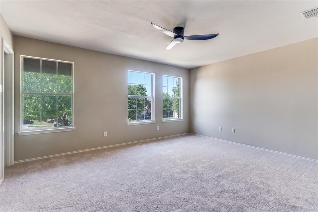 Neutral-toned interior space featuring wall-to-wall carpeting, three multi-pane windows, and a ceiling-mounted fan with integrated lighting