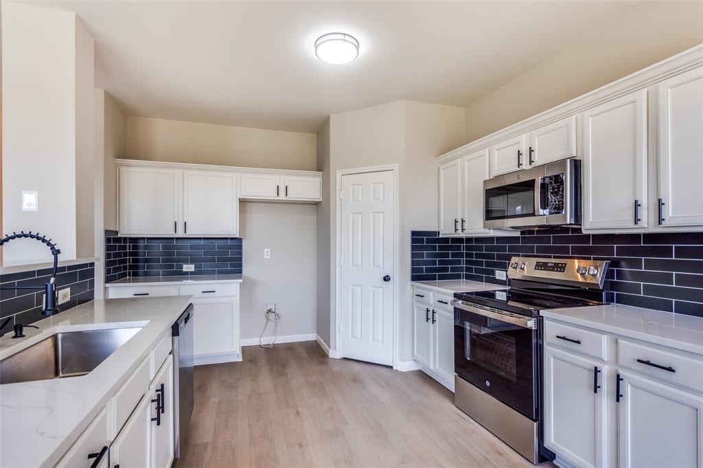 Kitchen featuring white shaker-style cabinetry, contrasting dark subway tile backsplash, light-toned solid surface countertops, stainless steel appliances, and wood-finish flooring