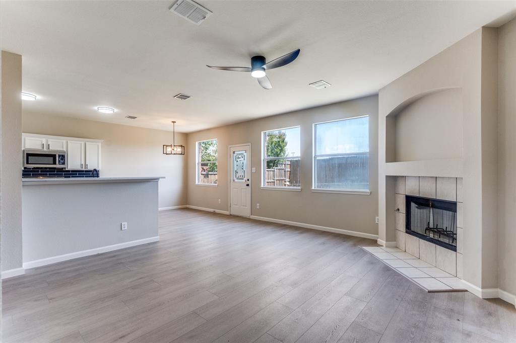 Open floor plan featuring wood-finish flooring, a fireplace with a tiled surround, a breakfast bar, and a ceiling fan