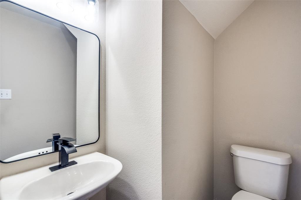 Wall-mounted rectangular mirror with rounded corners, pedestal sink, matte black single-handle faucet, and two-piece toilet