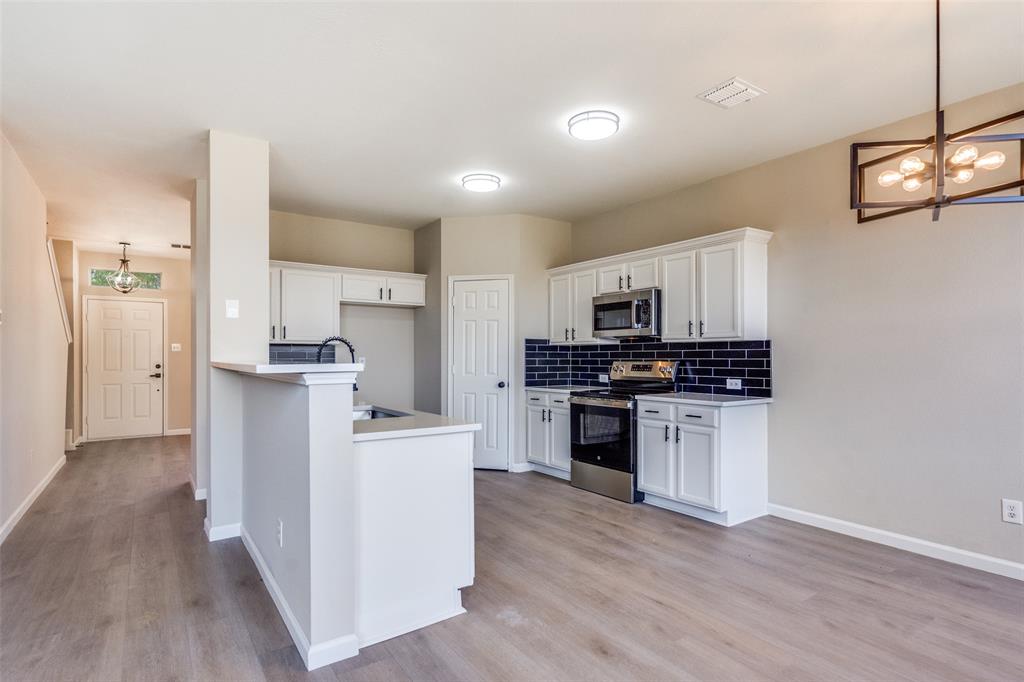 Kitchen featuring white shaker-style cabinetry, dark tiled backsplash, stainless steel appliances, wood-finish flooring, and a multi-light geometric chandelier