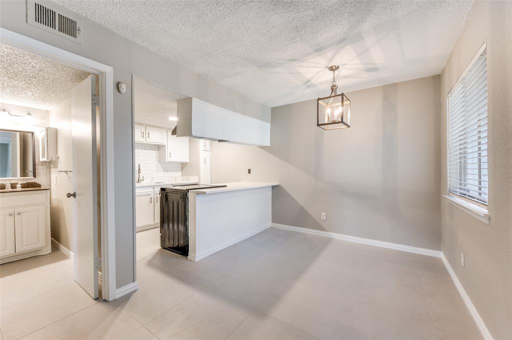 Open-concept area featuring neutral wall paint, tile flooring, a geometric pendant light fixture, a breakfast bar with white cabinetry, and horizontal window blinds