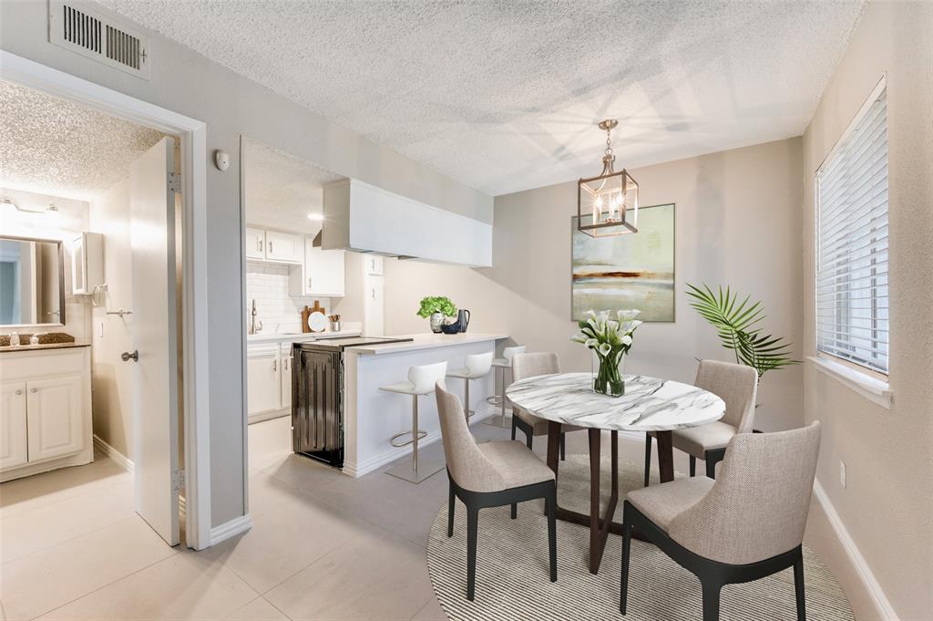 Kitchen featuring a breakfast bar, white cabinetry, and tile flooring, paired with an eating area highlighted by a geometric pendant light fixture and horizontal blinds