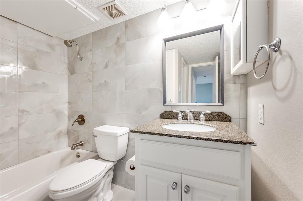 Bathroom featuring full-height floor to ceiling tile surround, white cabinetry, speckled stone vanity countertop, oval under-mount sink, and framed vanity mirror