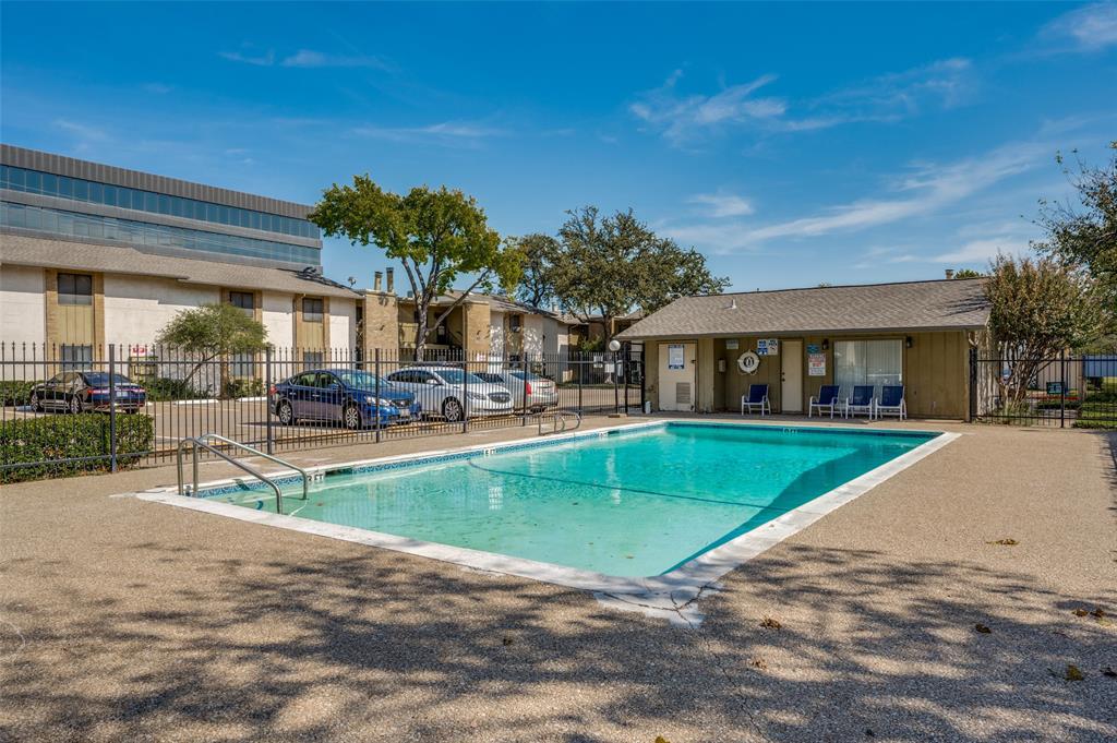 In-ground swimming pool with a concrete deck, metal perimeter fencing, and an adjacent community building