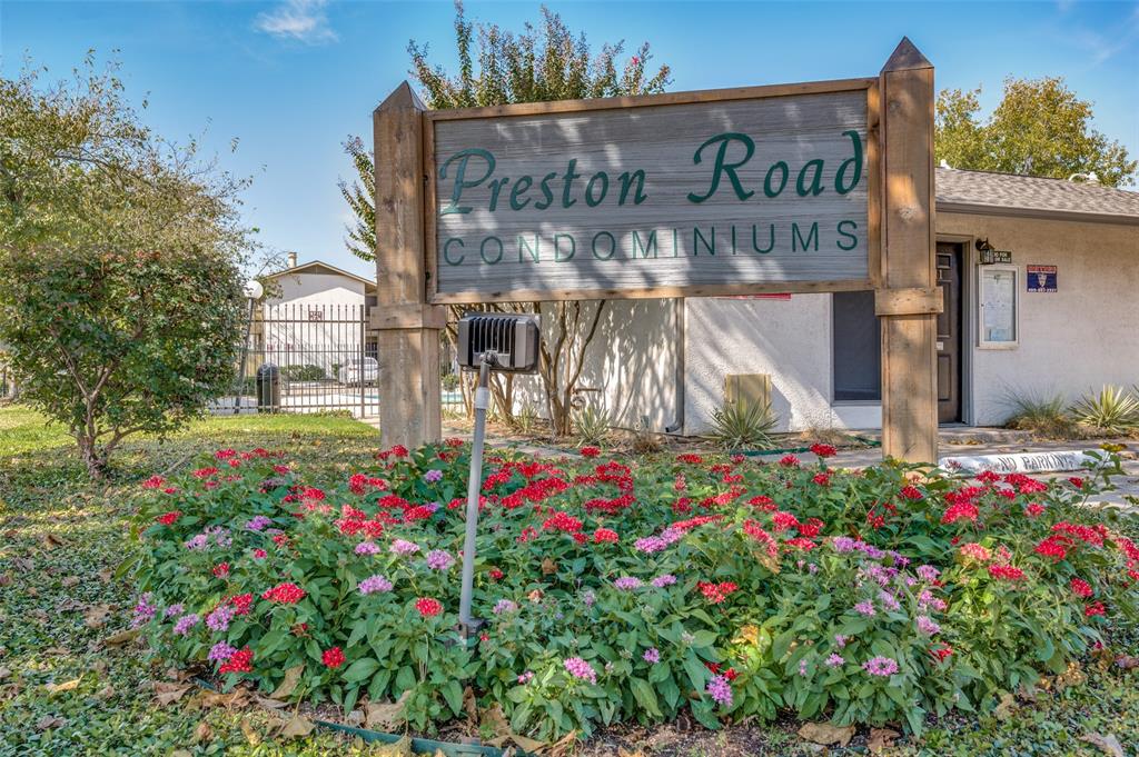 Entry sign for Preston Road Condominiums featuring a wooden post-and-beam structure with integrated directional lighting and established, flowering landscaping