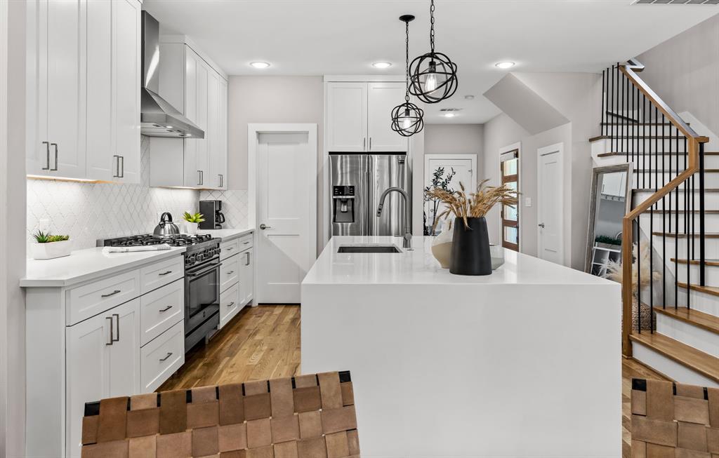 Kitchen featuring stainless steel refrigerator with ice dispenser, light hardwood / wood-style flooring, an island with sink, wall chimney exhaust hood, and range with gas cooktop