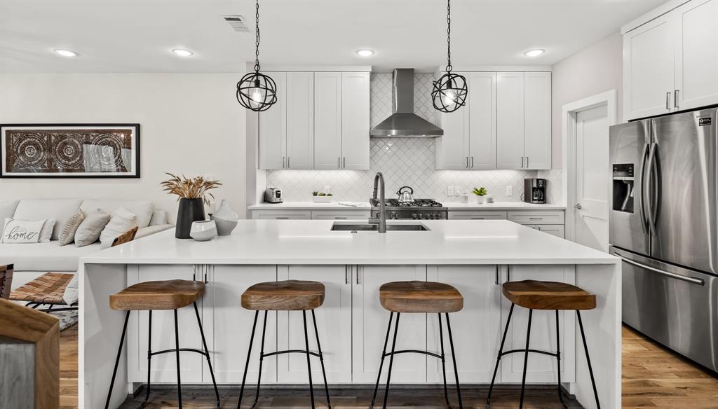 Kitchen with wall chimney exhaust hood, a breakfast bar, hardwood / wood-style flooring, and stainless steel fridge with ice dispenser