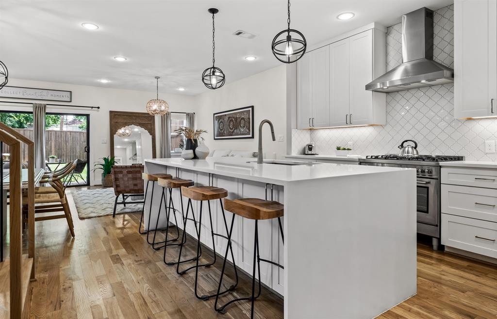 Kitchen featuring an island with sink, light wood-type flooring, stainless steel stove, wall chimney exhaust hood, and sink