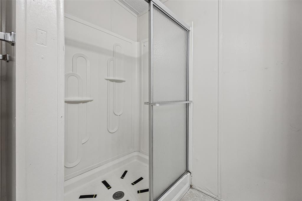 Shower stall featuring an integrated white surround with molded shelving, a textured sliding glass door, and a shower pan with slip-resistant treads