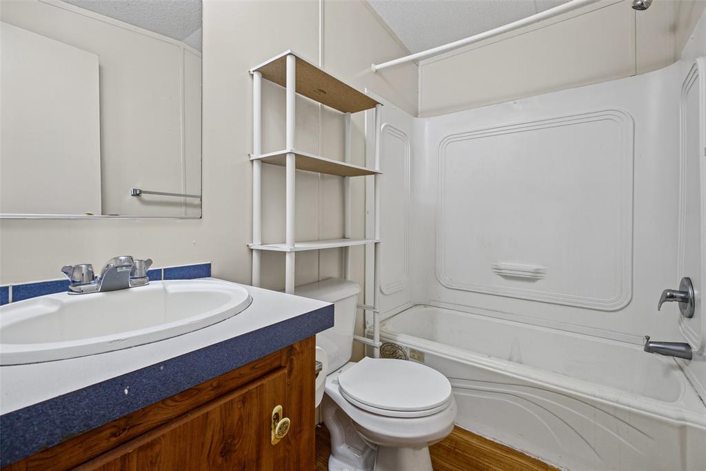 Bathroom featuring a wood-finish vanity with a molded sink, blue countertop surfacing, and a white one-piece shower and tub surround