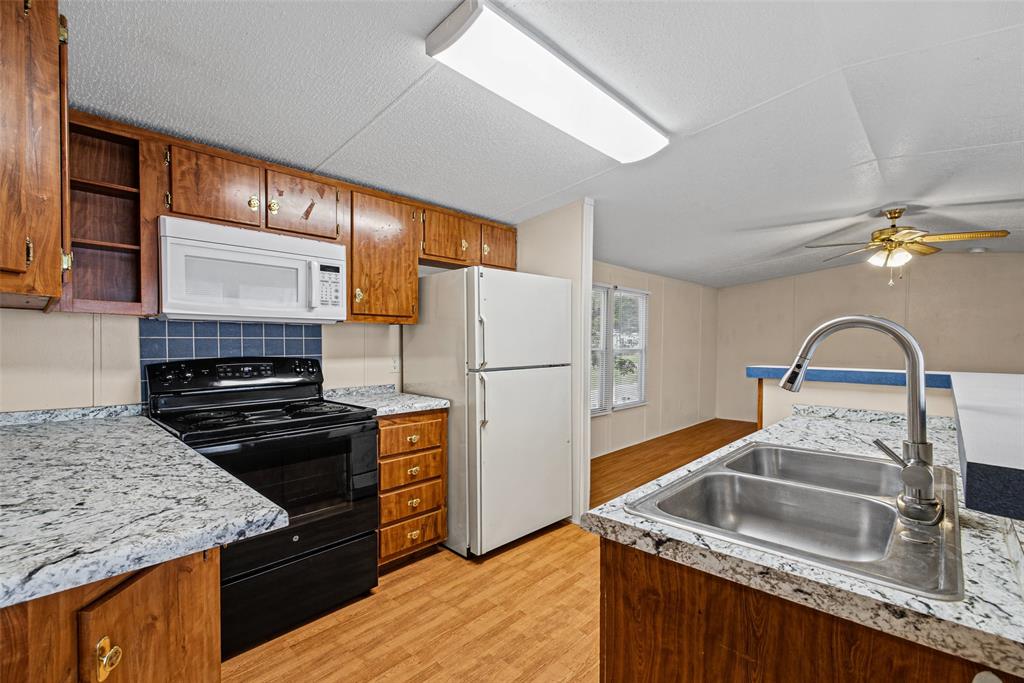 Kitchen featuring wood-finish cabinetry, patterned laminate countertops, stainless steel double-basin sink with arched faucet, and built-in appliances
