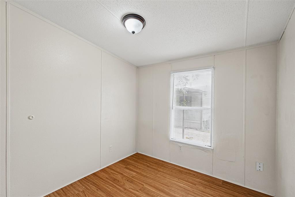 Interior room featuring wood-finish flooring, white panel walls, a single-window configuration with horizontal blinds, and a dome-style flush-mount ceiling fixture