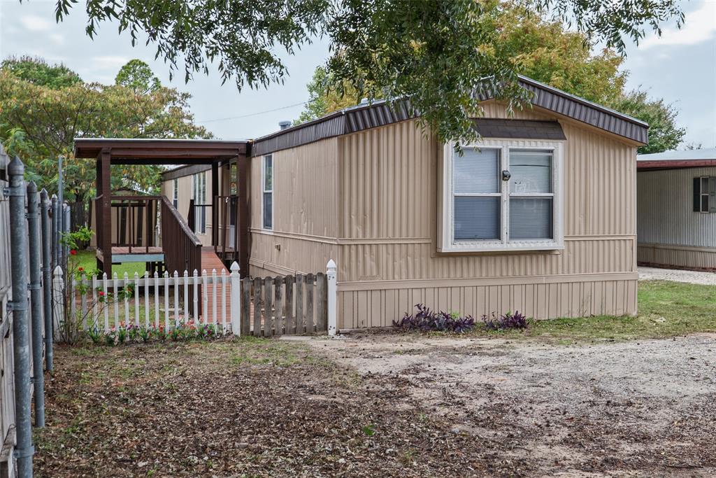 Exterior featuring vertical metal siding, a covered entryway, elevated wooden deck, and a picket fence enclosure