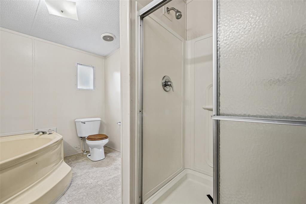 Bathroom featuring a corner soaking tub, a separate shower stall with a framed sliding glass door, a toilet, and neutral-toned flooring