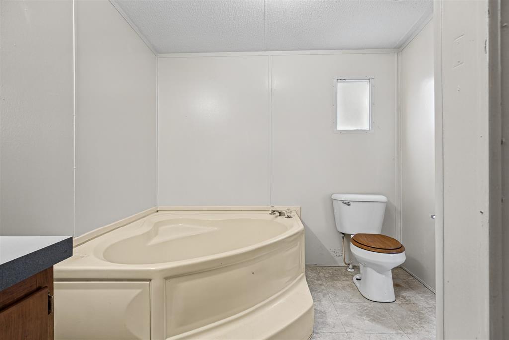 Corner soaking tub with integrated stairs, white porcelain toilet, and neutral-tone flooring
