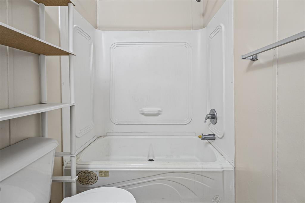 White acrylic tub-and-shower surround with integrated molded shelving, chrome-finish single-handle faucet, and attached metal towel bar