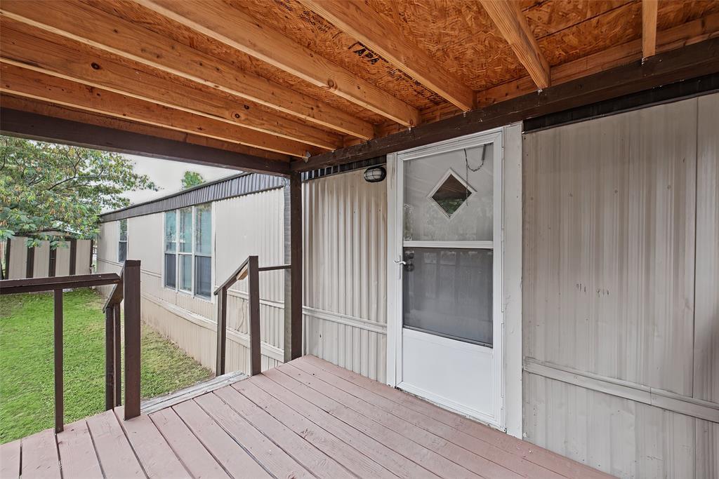 Covered outdoor deck with an exposed wood-beam ceiling, integrated railing, and diamond-pane entry door