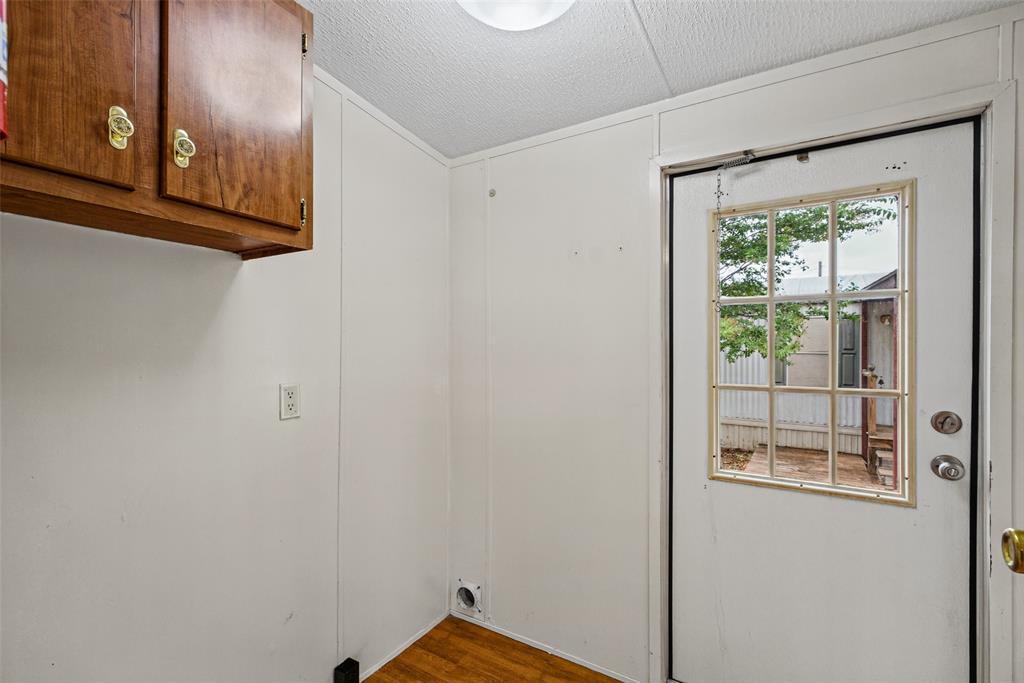 Utility area featuring wood-finish flooring, wall-mounted wood cabinetry with brass-tone hardware, and an exterior door with a nine-pane window