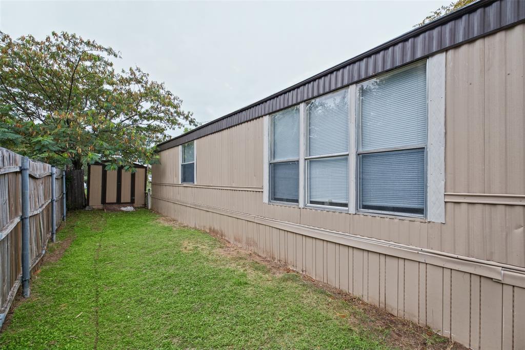 Exterior elevation featuring vertical metal siding, multi-pane windows, wood-style privacy fencing, and a detached storage structure