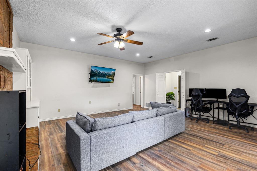Living area featuring wood-finish flooring, a textured ceiling with a central fan, recessed lighting, and a brick-accented wall with built-in cabinetry