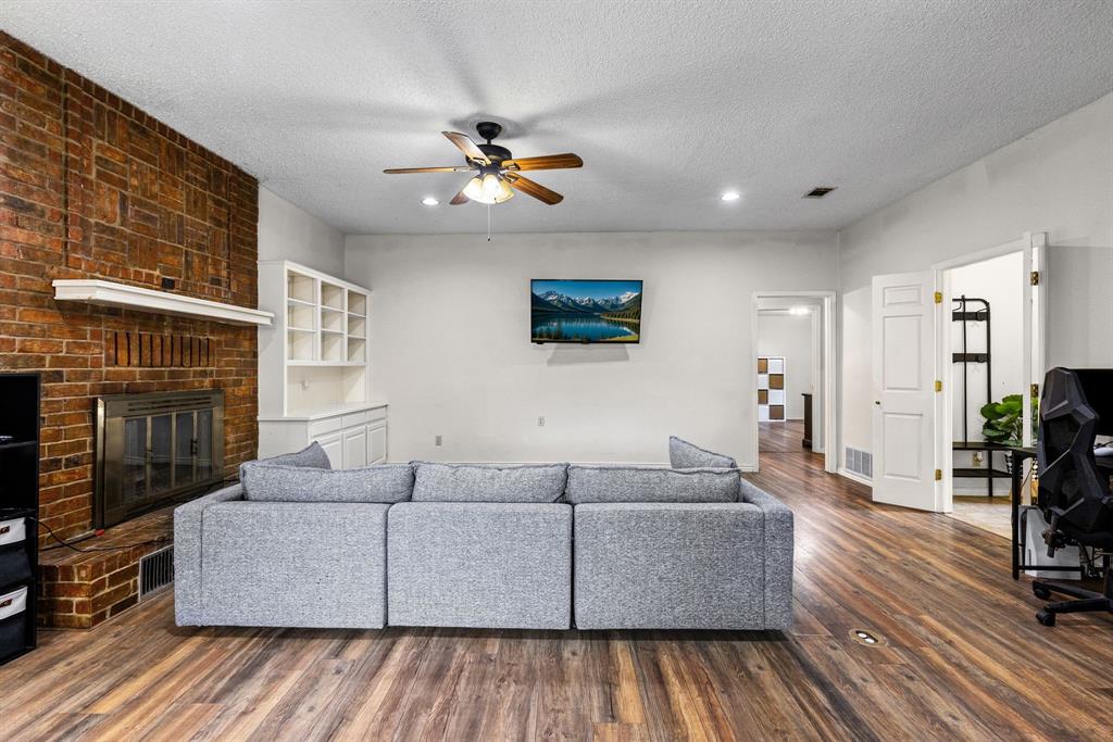 Full-height brick fireplace with a mantle and built-in shelving, wood-finish flooring, and a ceiling fan with integrated lighting