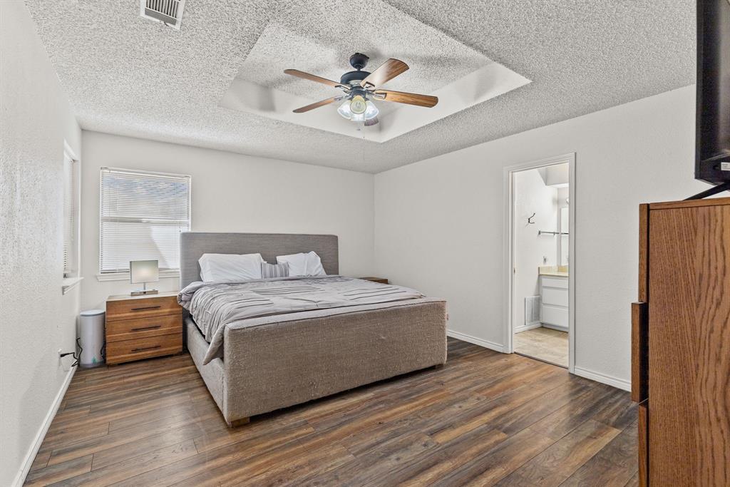 Bedroom featuring a tray ceiling with a central multi-blade ceiling fan and wood-finish flooring