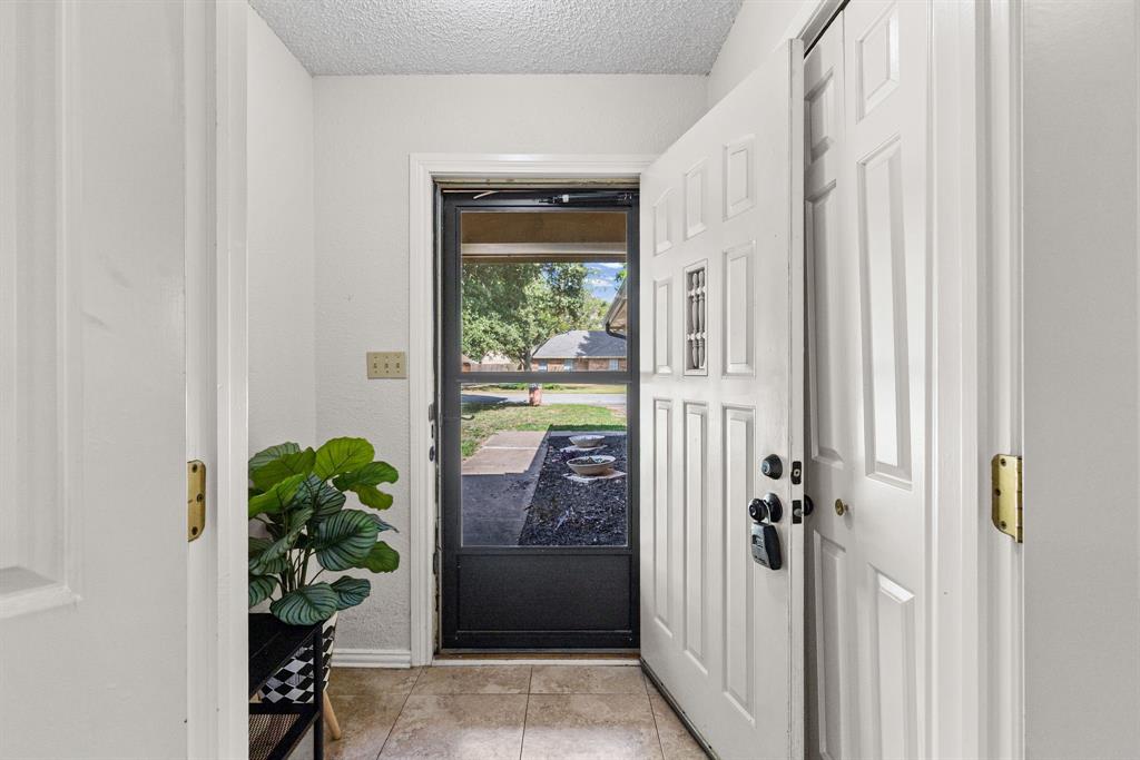 Entryway featuring a white paneled door with a decorative inset window, a glass-panel storm door, and neutral tile flooring