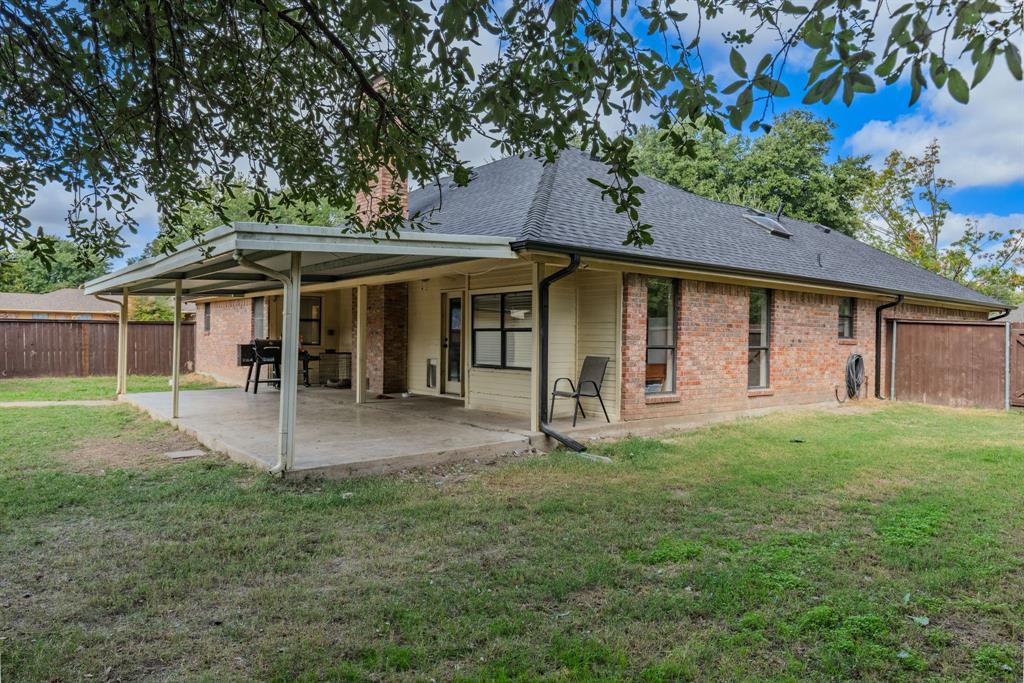 Rear exterior featuring a brick and siding facade, a covered patio, a chimney, a shingled roof, and a fenced backyard