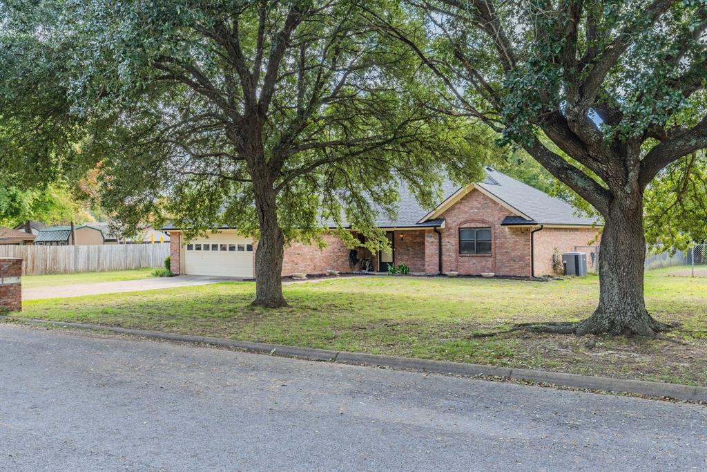 Single-story brick exterior featuring a multi-gabled roofline, an attached two-car garage, and mature shade trees