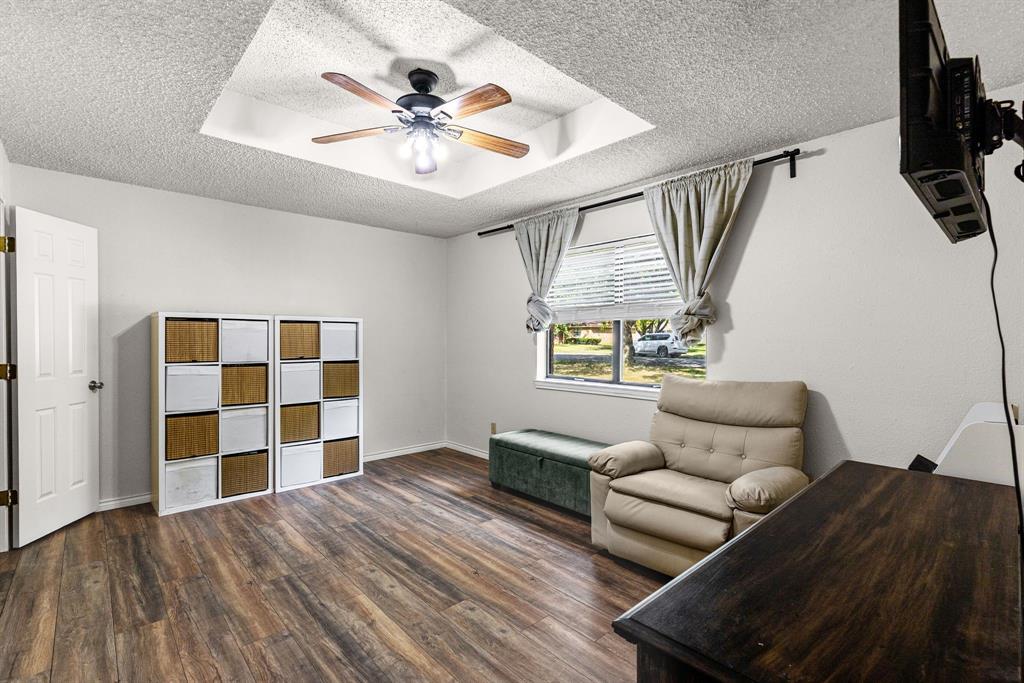 Room featuring wood-finish flooring, a tray ceiling, and a central ceiling fan with integrated lighting