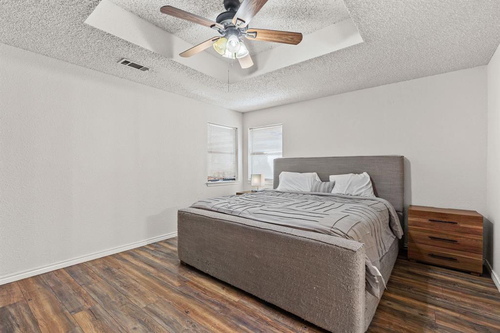 Room featuring wood-finish flooring, a tray ceiling with a center-mounted ceiling fan, and dual windows