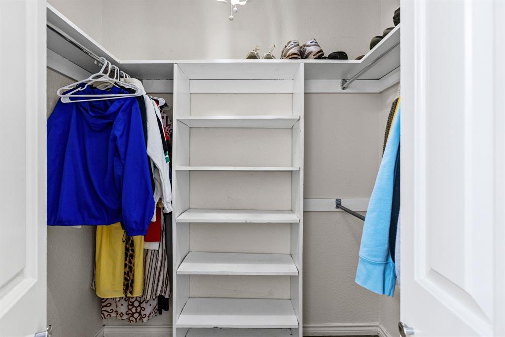 Walk-in closet featuring white built-in shelving, dual hanging rods, and an overhead shelf