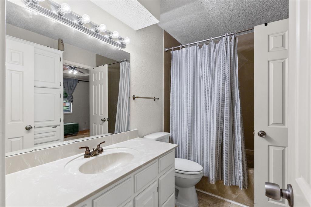 Bathroom featuring a stone-composite countertop with an integrated oval basin, white shaker-style cabinetry, wall-mounted multi-bulb light fixture, and a tile-surround shower enclosure