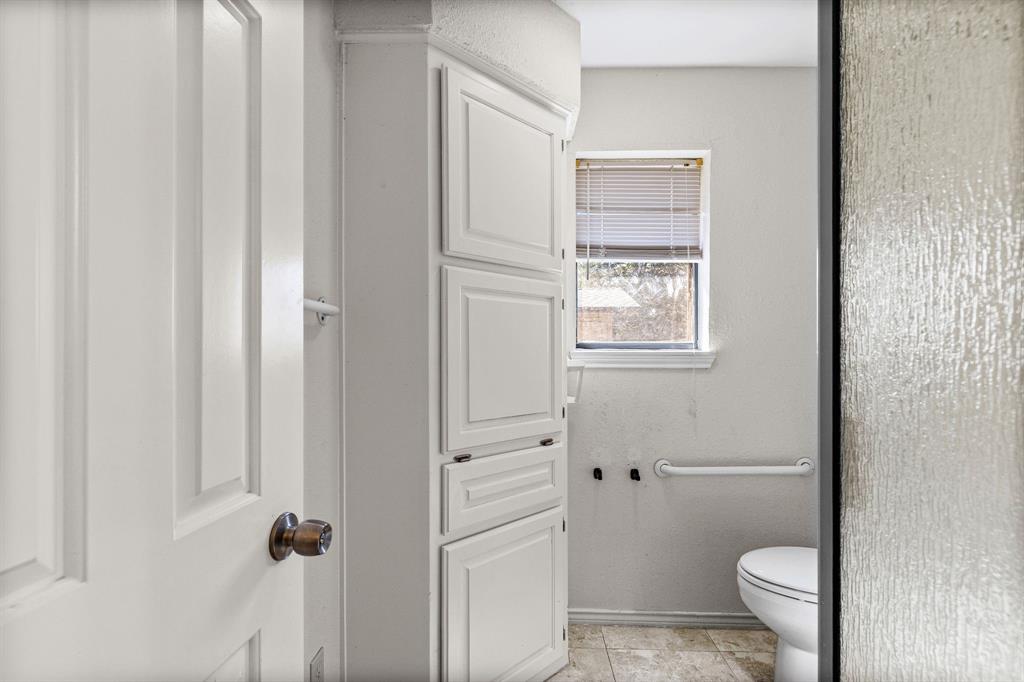 Built-in floor-to-ceiling cabinetry, neutral tile flooring, and wall-mounted grab bar
