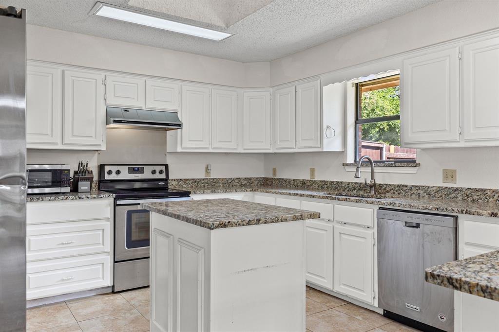 Kitchen featuring white shaker-style cabinetry, stone-finish countertops, central island, stainless steel appliances, and tile flooring