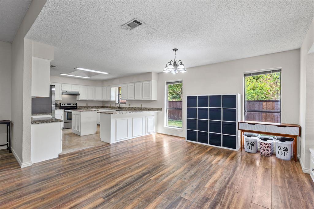 Open-concept kitchen and living area featuring wood-finish flooring, white cabinetry, stone-surface countertops, and multi-pane windows