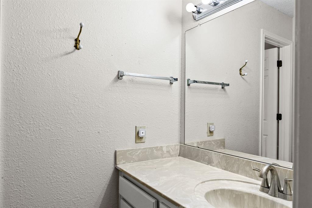Vanity featuring a stone-patterned countertop with an integrated basin, a polished metal faucet, a large frameless mirror, and a multi-bulb light fixture
