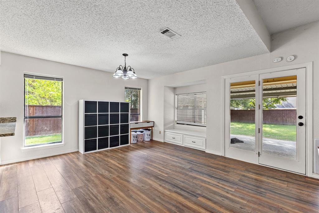 Wood-finish flooring, built-in window seating with cabinetry storage, double French doors, and multi-light chandelier fixture
