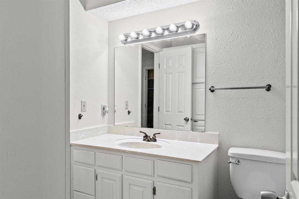 Bathroom vanity featuring white cabinetry, a solid-surface countertop with an integrated basin, a large rectangular mirror, and a multi-bulb vanity light fixture