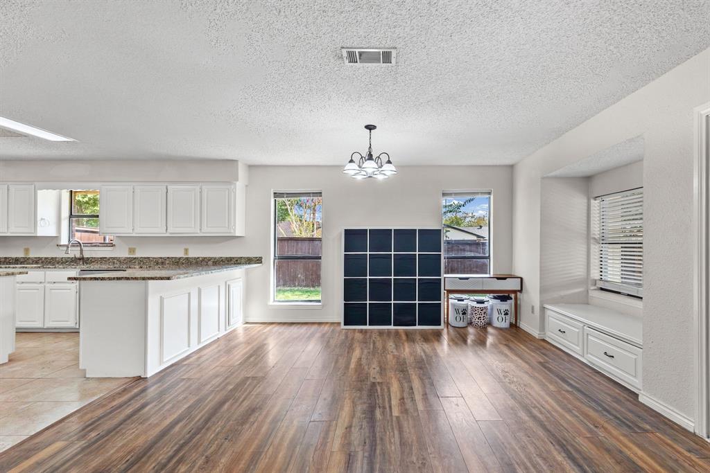 Kitchen area featuring white cabinetry, stone-surface countertops, wood-finish flooring, a multi-arm chandelier, and a built-in window seat with storage drawers