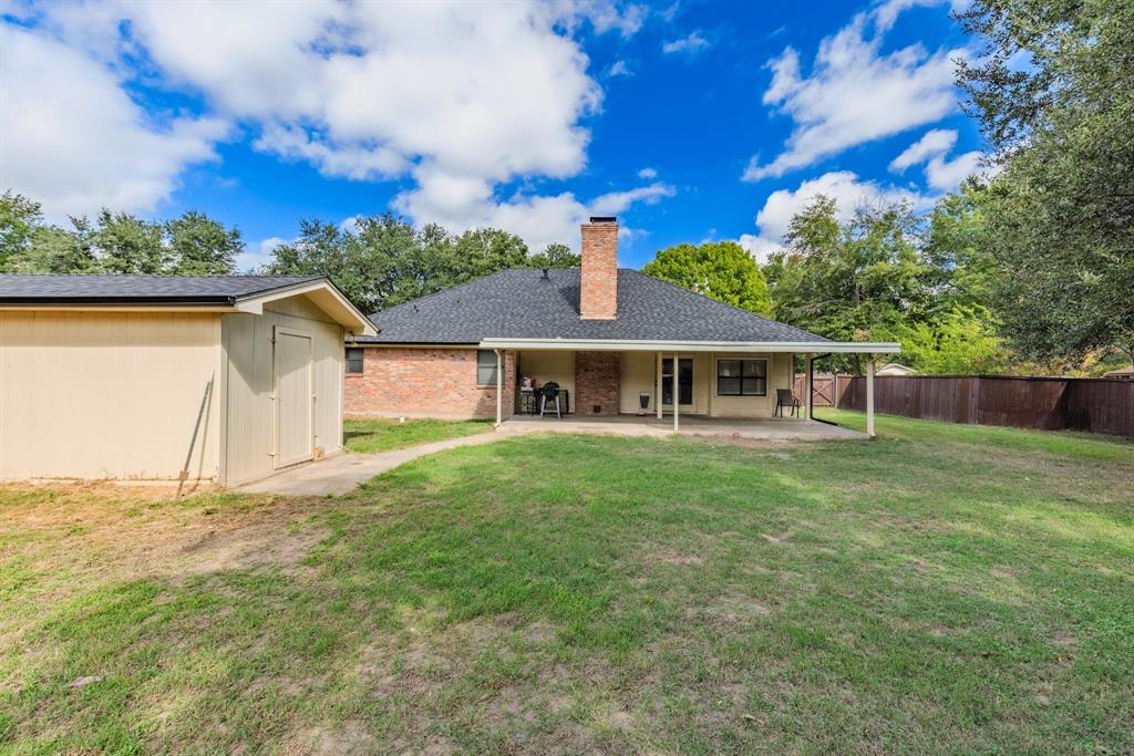 Expansive backyard featuring a covered patio, brick exterior chimney, detached storage building, and perimeter wood fencing