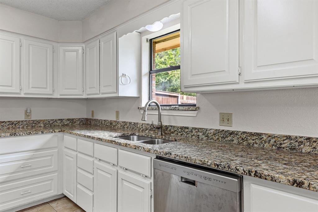 Kitchen featuring white cabinetry, stone-finish countertops, stainless steel dual-basin sink with pull-down faucet, and integrated dishwasher