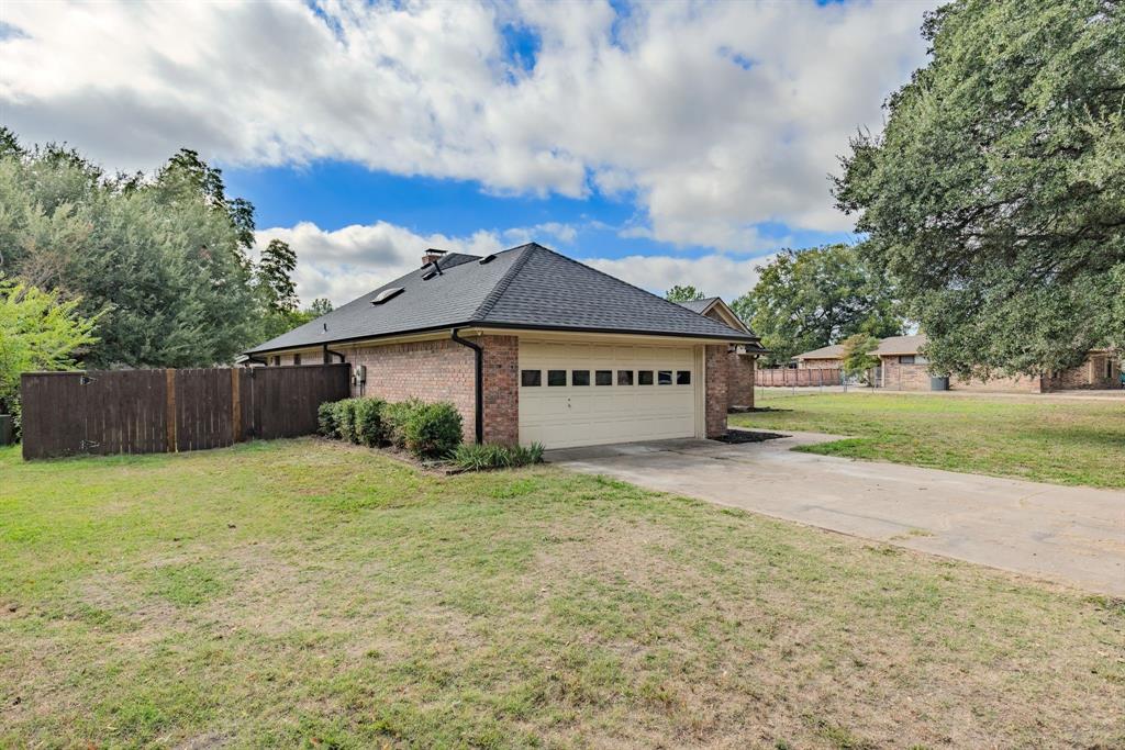 Brick exterior with a multi-paneled garage door, asphalt shingle roof, skylights, and a wood-slat privacy fence