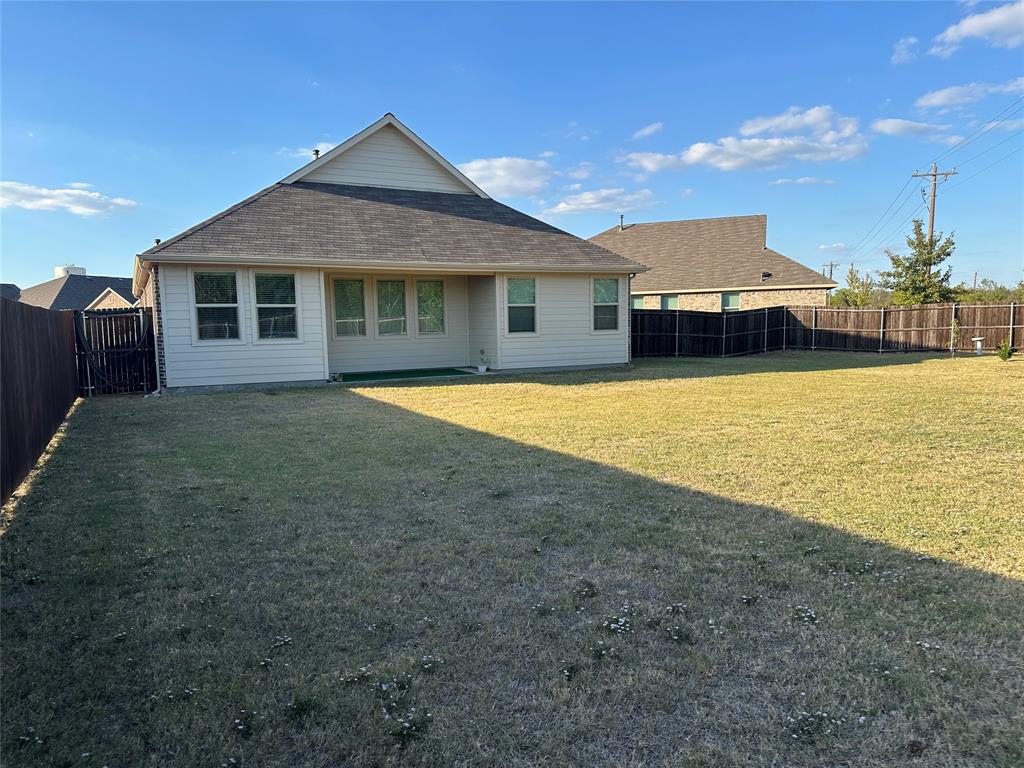 Expansive backyard featuring a leveled lawn, tall wood-panel privacy fencing, and exterior siding with a gabled roofline