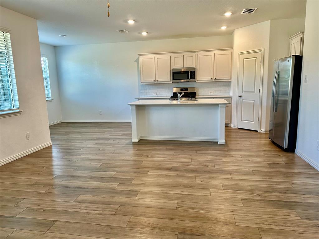 Kitchen featuring white cabinetry, quartz-topped center island, wood-finish flooring, stainless steel appliances, and subway tile backsplash