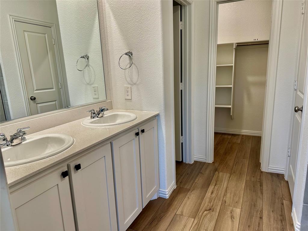 Double vanity with dual drop-in sinks, stone-finish countertops, wood-finish flooring, and a walk-in storage area featuring built-in shelving
